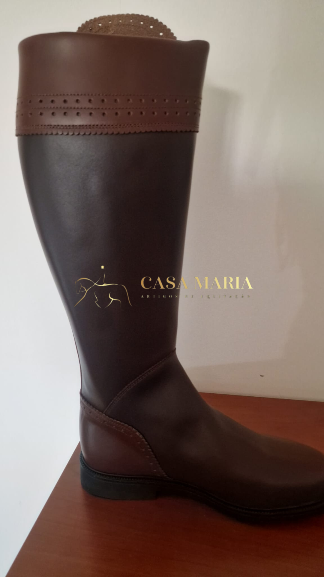 Bota alta castanha escura em pele para equitação com acabamento superior perfurado em castanho mais claro.