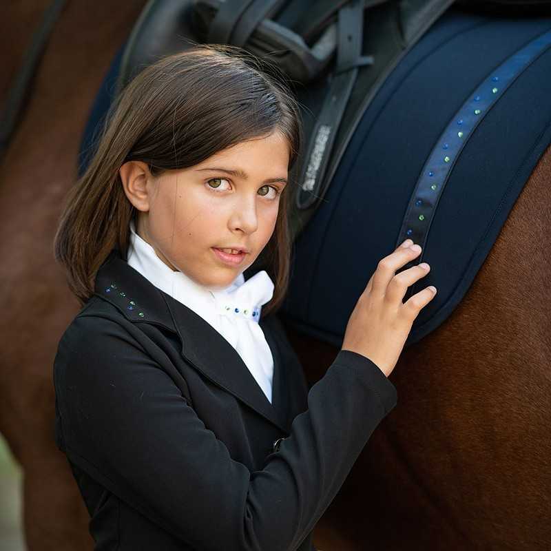 Criança com casaco preto e camisa branca ao lado de cavalo com manta azul escura