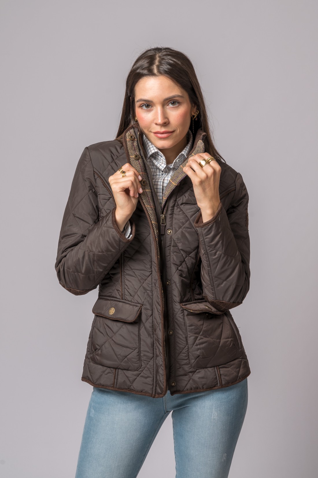 Mulher com casaco castanho acolchoado e camisa xadrez em fundo cinzento