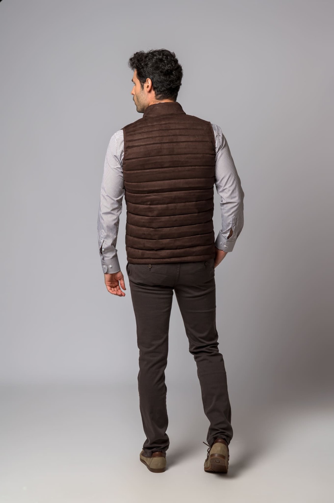 Homem de costas com colete acolchoado castanho e camisa às riscas
