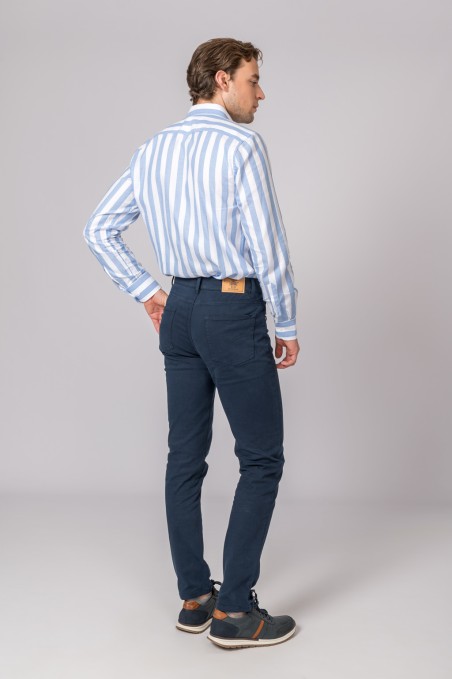 Homem visto de costas a usar calças azuis justas e camisa às riscas azul claro e branco.