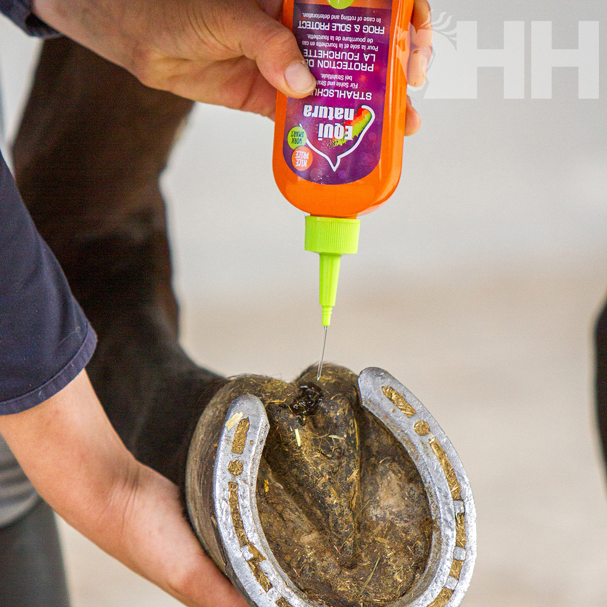 Aplicação de líquido protetor numa ferradura metálica por mão com frasco laranja e verde