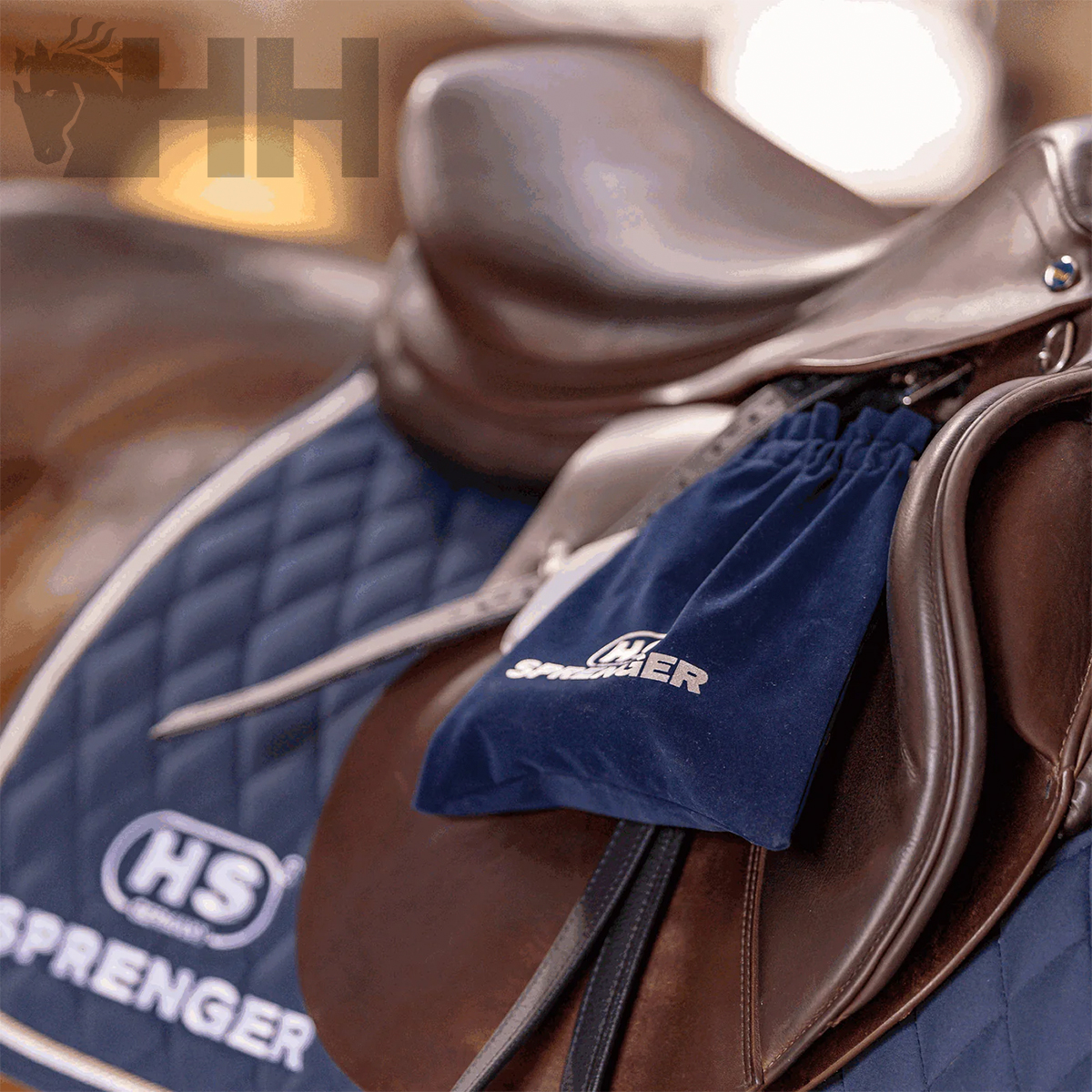 Sela de cavalo castanha sobre manta azul acolchoada com saco azul e texto HS SPRENGER