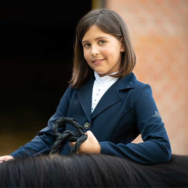 Menina com blusão azul escuro e camisola branca segurando rédeas pretas junto a um cavalo
