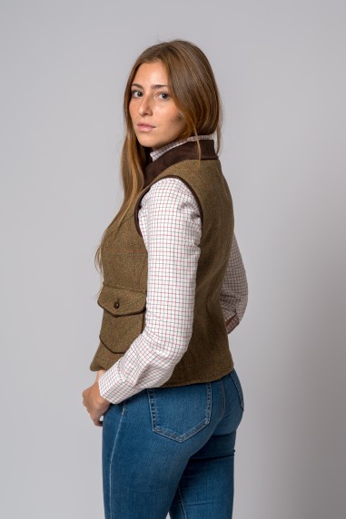 Mulher de lado com colete castanho de tweed, camisa xadrez branca e calças de ganga azuis