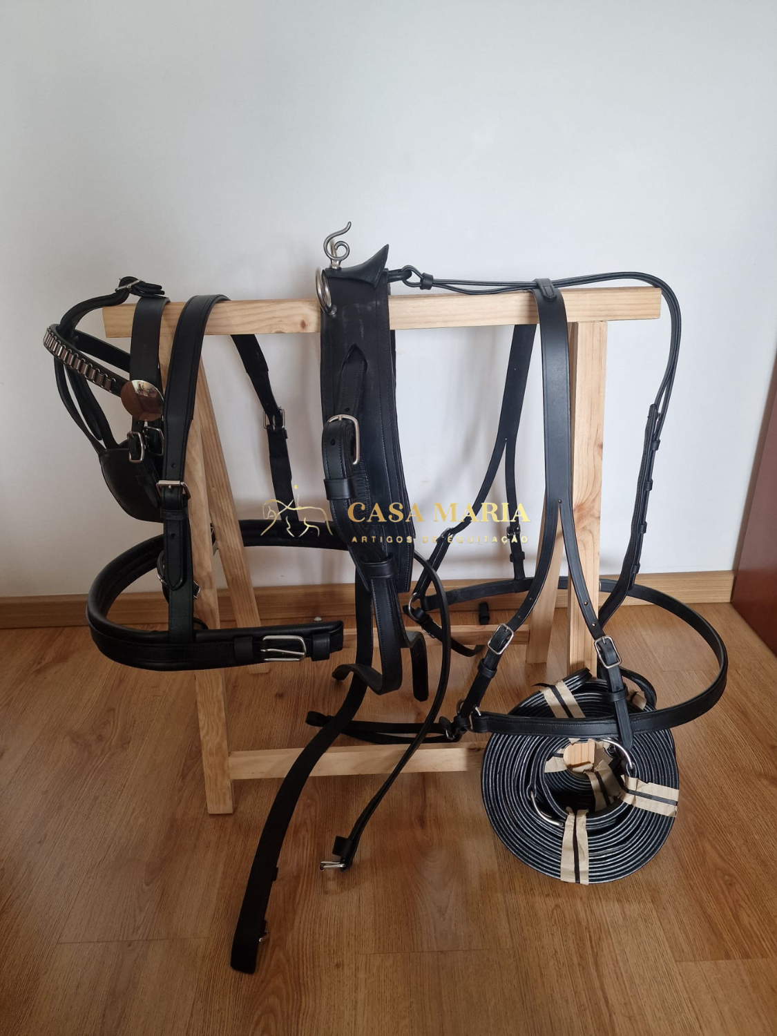 Conjunto de arreios pretos em pele pendurado numa estrutura de madeira