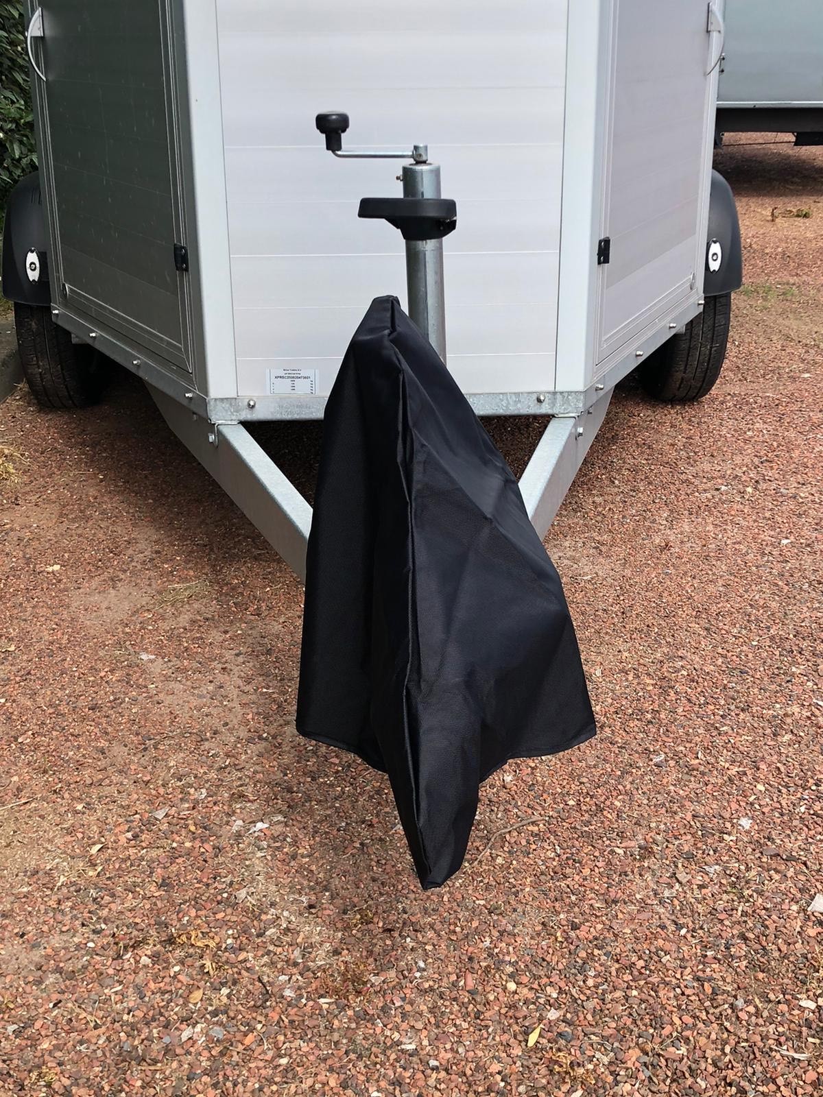 Reboque cinza com suporte metálico coberto por capa preta em terreno de cascalho