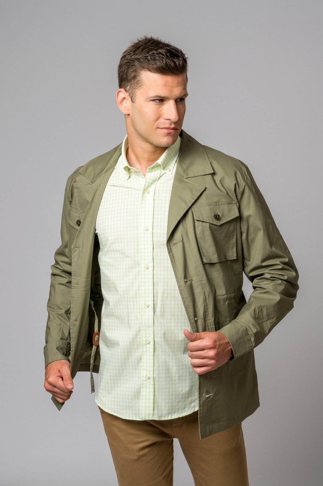 Homem com camisa verde claro e casaco verde-oliva em fundo cinza