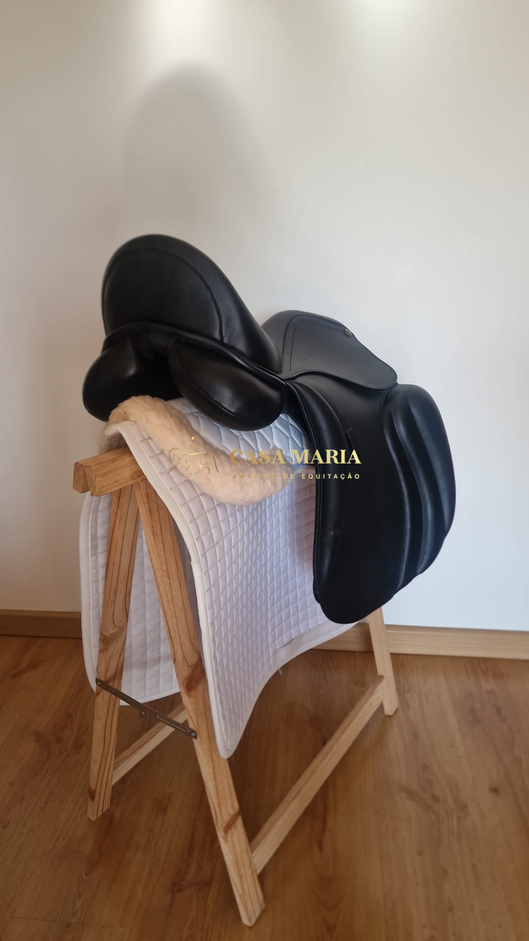 Sela preta de equitação sobre manta branca e suporte de madeira