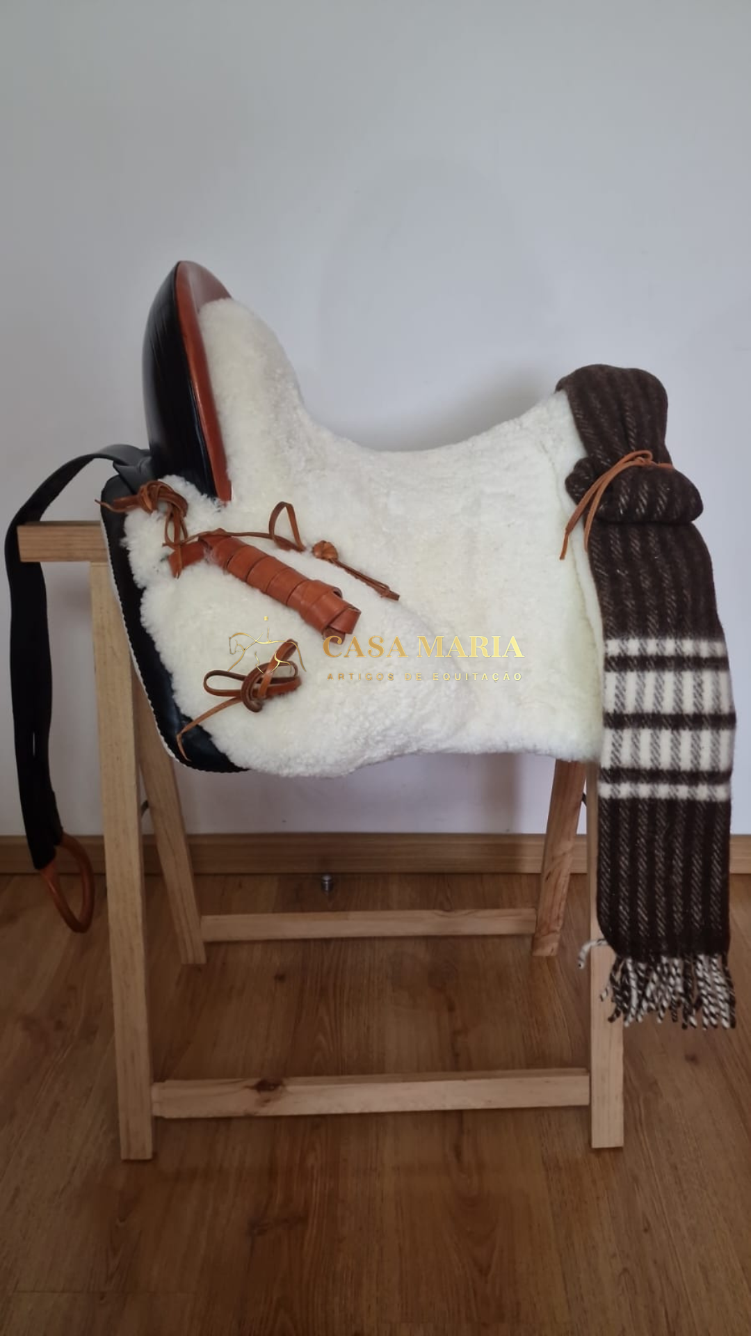 Sela branca em pelúcia com detalhes em couro castanho e manta castanha às riscas sobre suporte de madeira