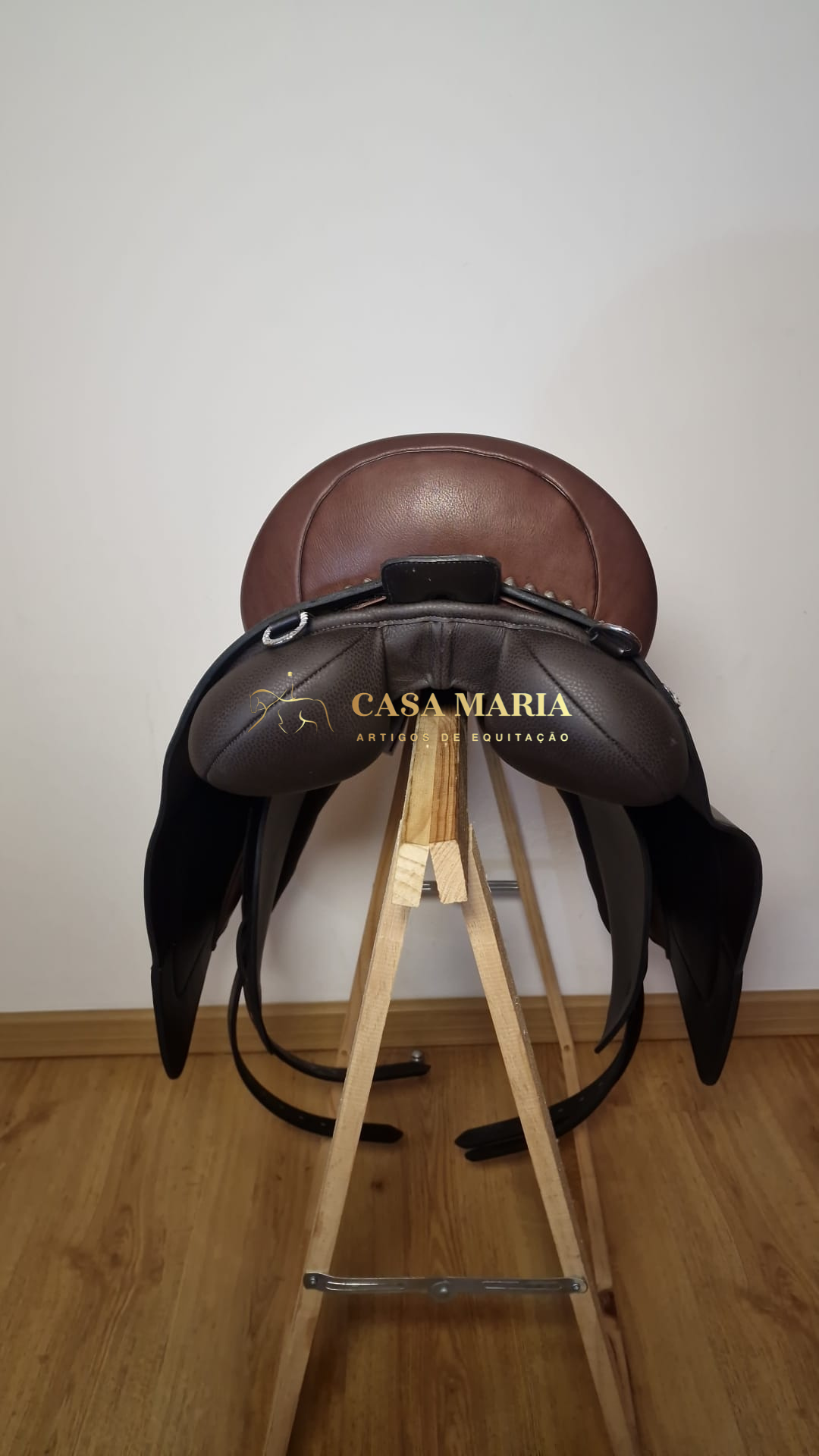 Sela de equitação em couro castanho sobre suporte de madeira em fundo branco