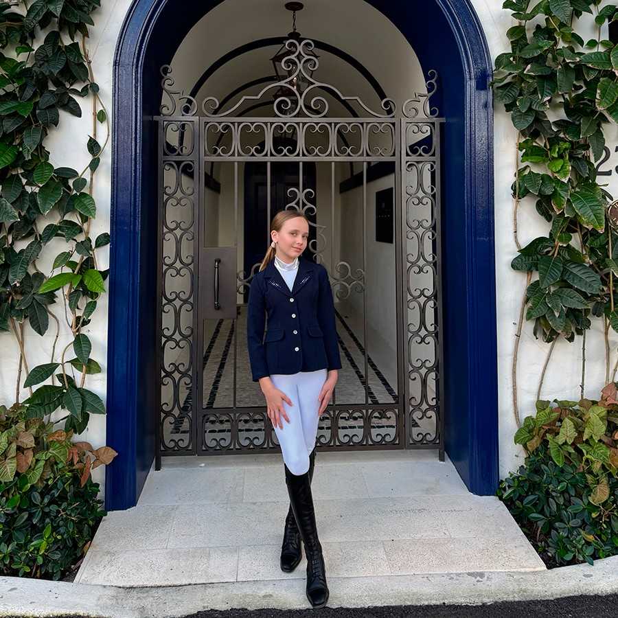 Menina com roupa de equitação diante de porta de ferro trabalhado