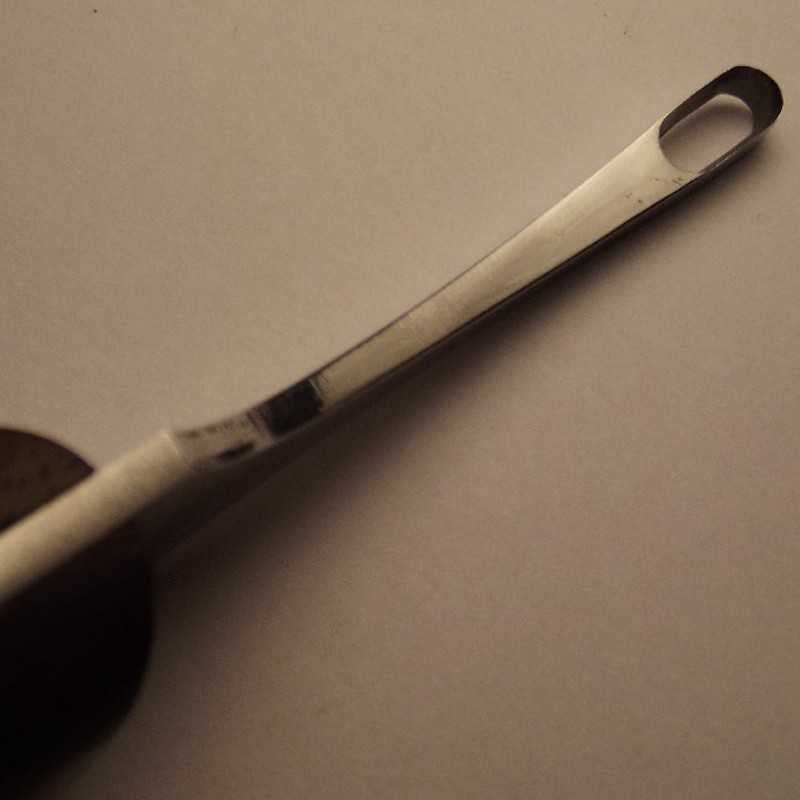 Colher de metal com pega com orifício oval sobre superfície bege