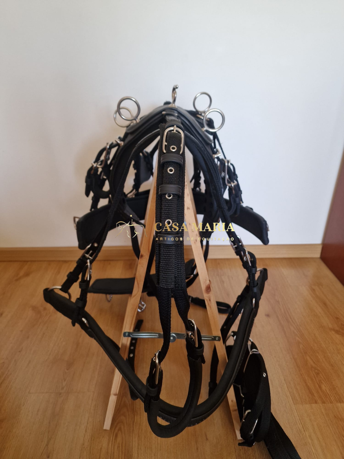 Arreio preto com ferragens metálicas em suporte de madeira sobre chão de parquet