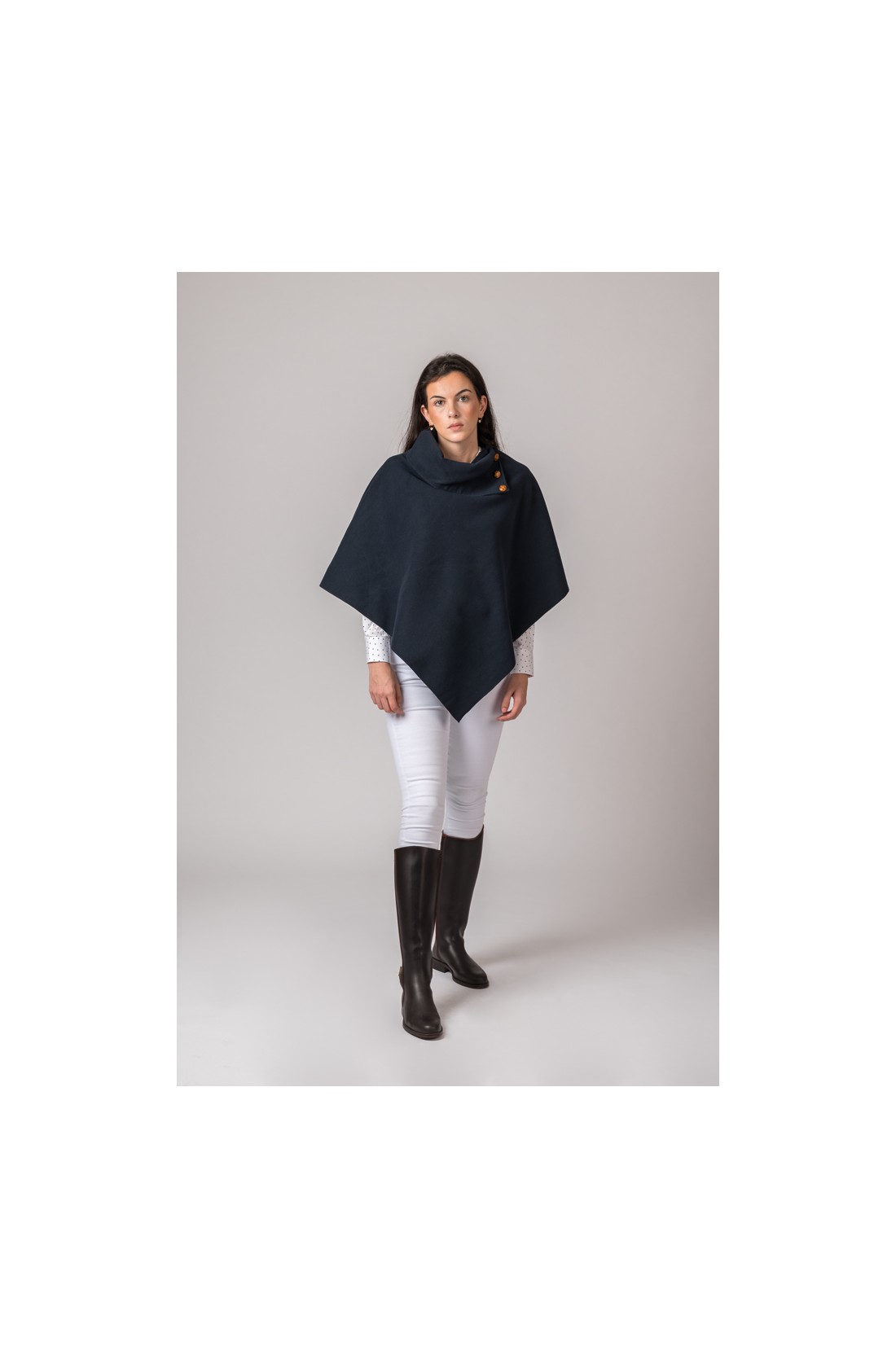 Mulher com poncho preto com botões, calças brancas e botas pretas