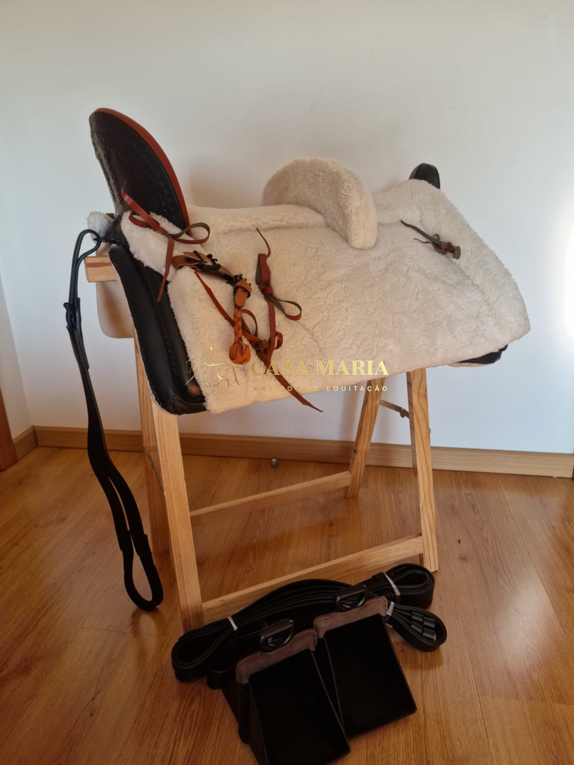 Sela de equitação branca e castanha com estribos pretos em suporte de madeira