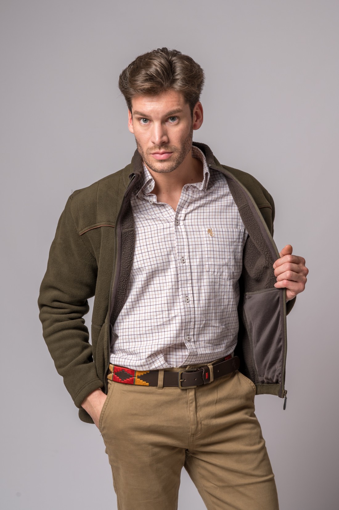 Homem com camisa de padrão quadrado, casaco verde, calças camel e cinto colorido