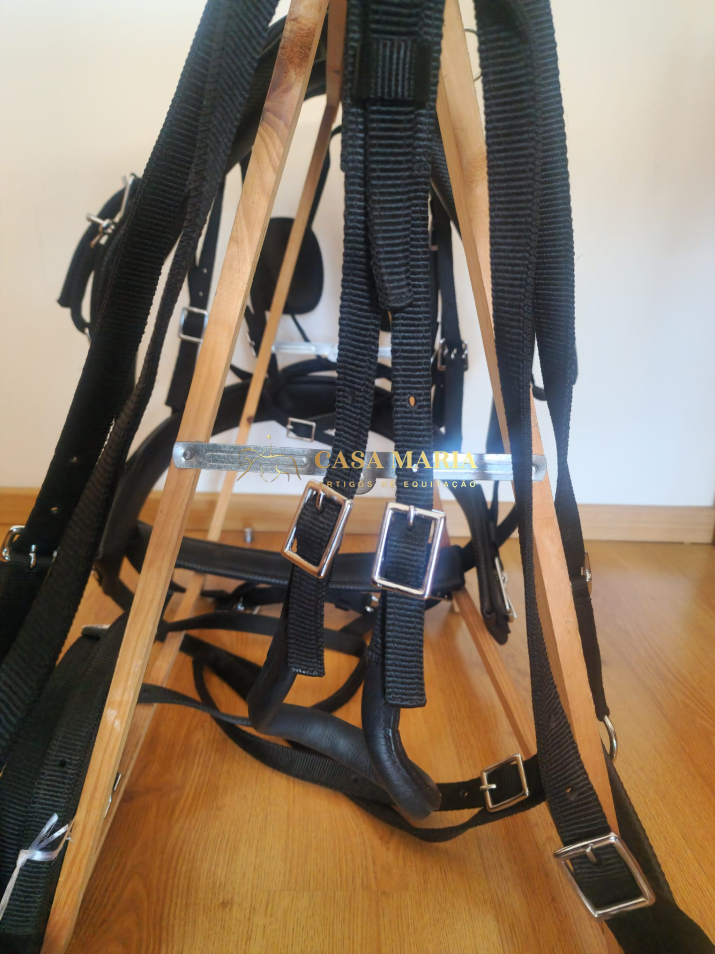 Arnês de cavalo preto com fivelas metálicas e suporte de madeira