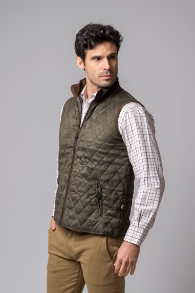 Homem com colete acolchoado verde, camisa xadrez branca e calças castanhas