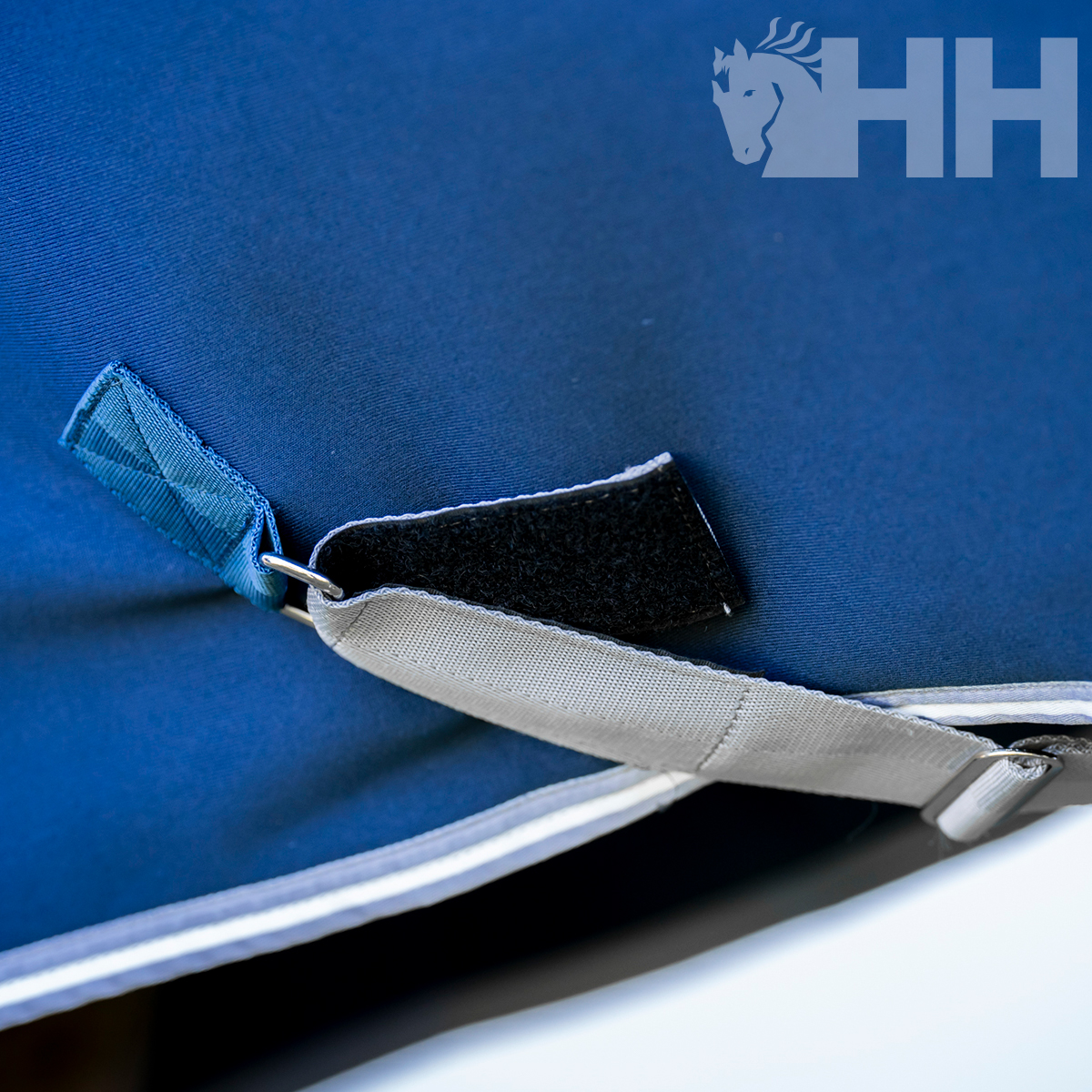 Fecho com velcro e argola numa capa têxtil azul com logótipo de cavalo e HH cinza