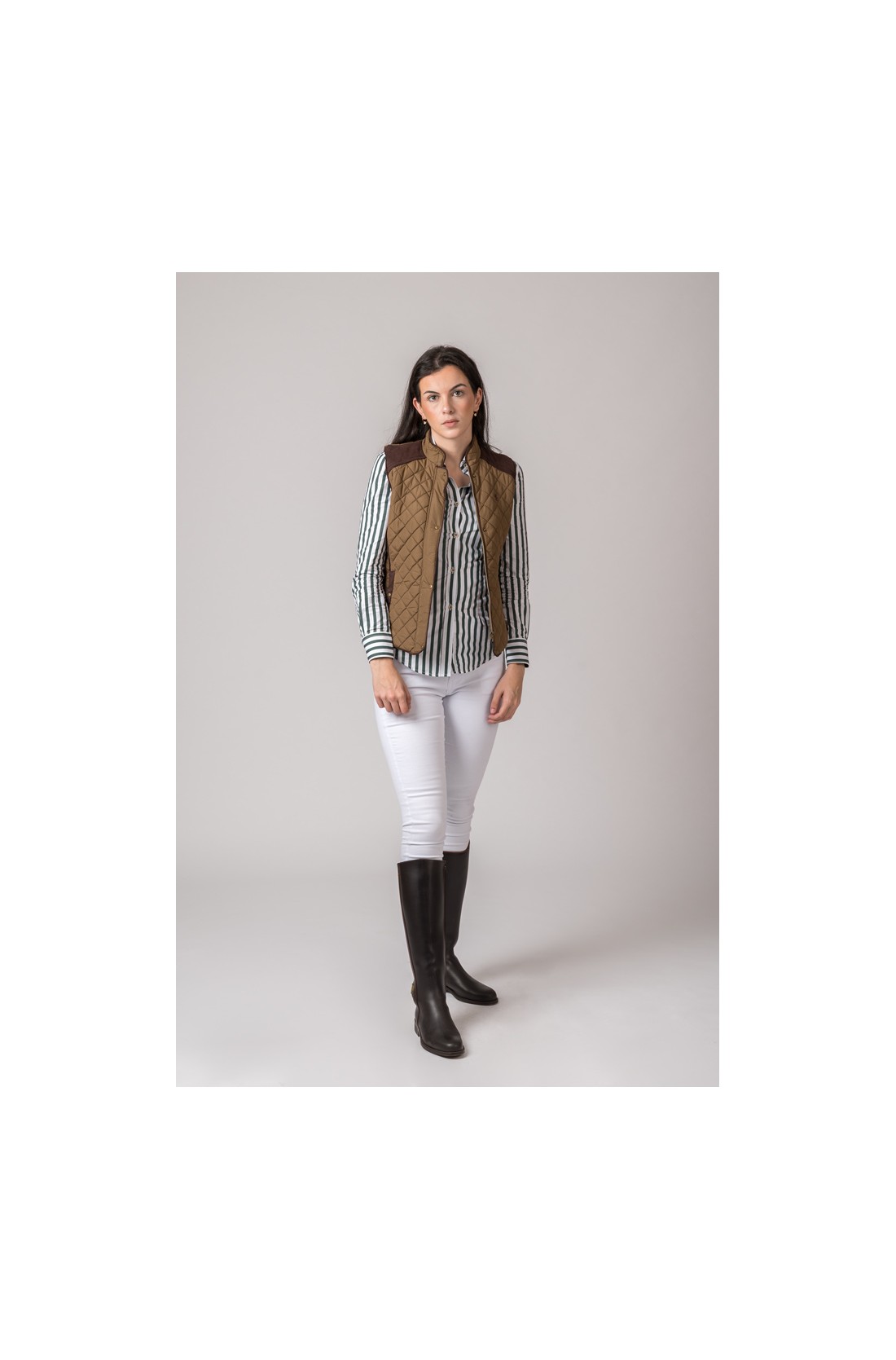 Mulher com colete castanho, camisa às riscas, calças brancas e botas pretas