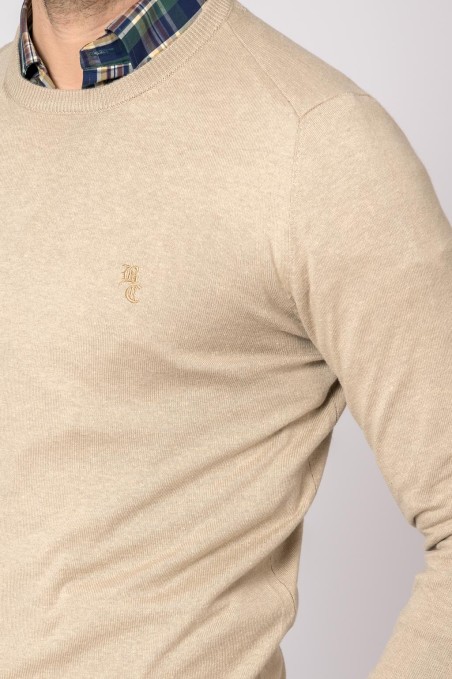 Suéter bege de malha com logotipo bordado, usado com camisa xadrez.