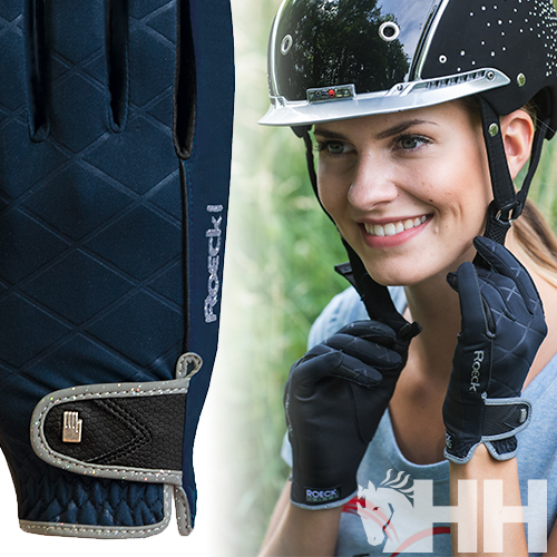 Mulher sorridente com capacete preto e luvas de equitação azul escuras com detalhes cinza e marca Roeckl