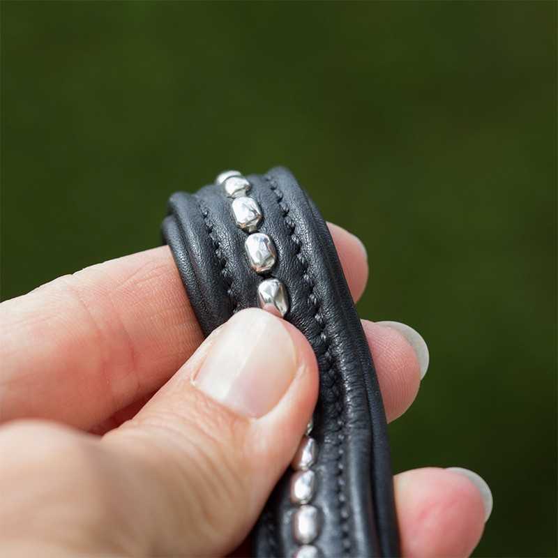 Pulseira preta de couro com metais prateados segurada por mão