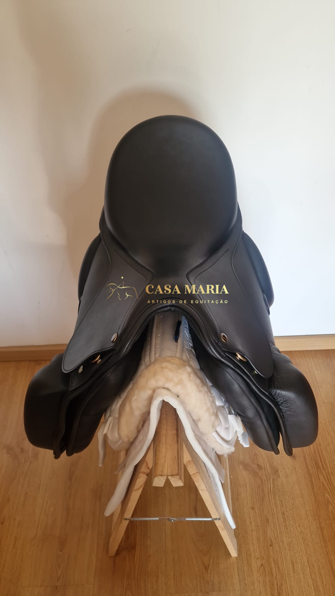 Sela de equitação preta em couro com almofadas brancas sobre suporte de madeira