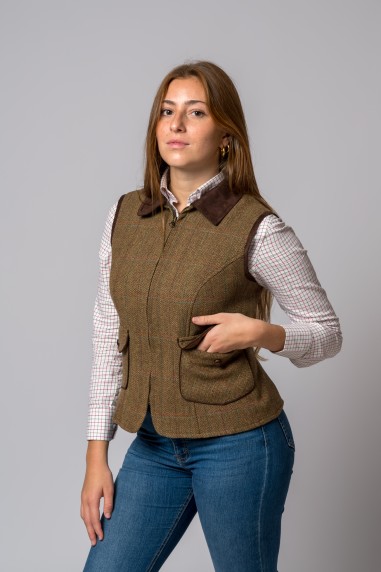 Mulher com colete castanho, camisa xadrez branca e jeans azul, fundo cinzento