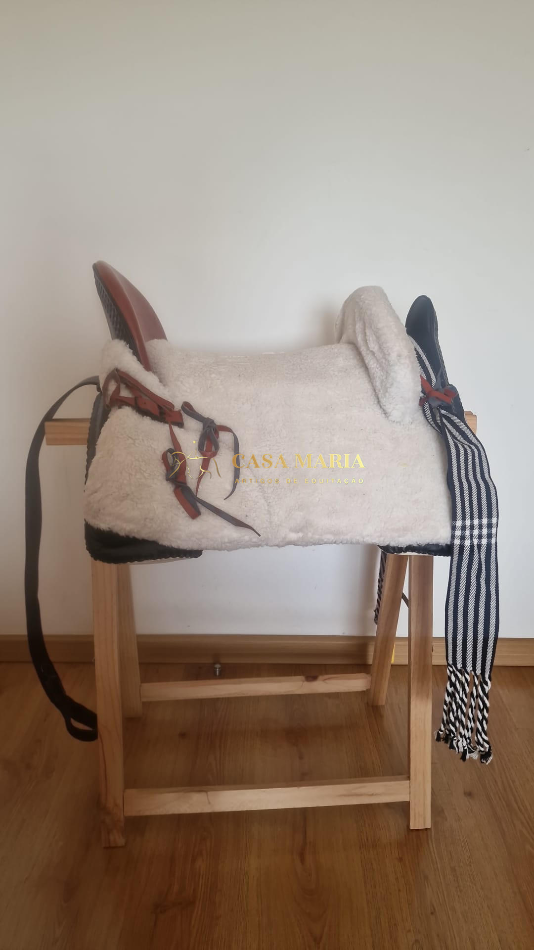 Sela de equitação branca com detalhes castanhos e pretos numa estrutura de madeira