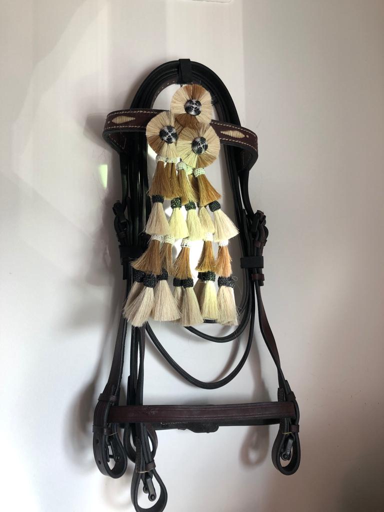 Cabresto em pele castanha escura com borlas bege e castanhas pendurado na parede