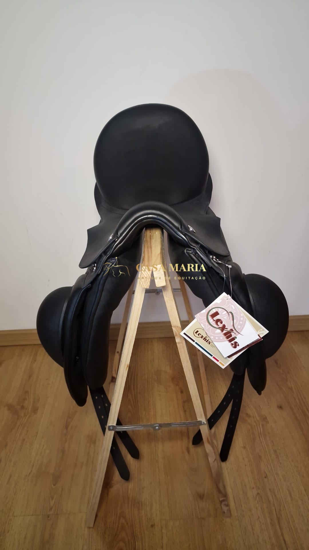 Sela de equitação preta em couro com etiqueta pendurada, colocada num suporte de madeira.