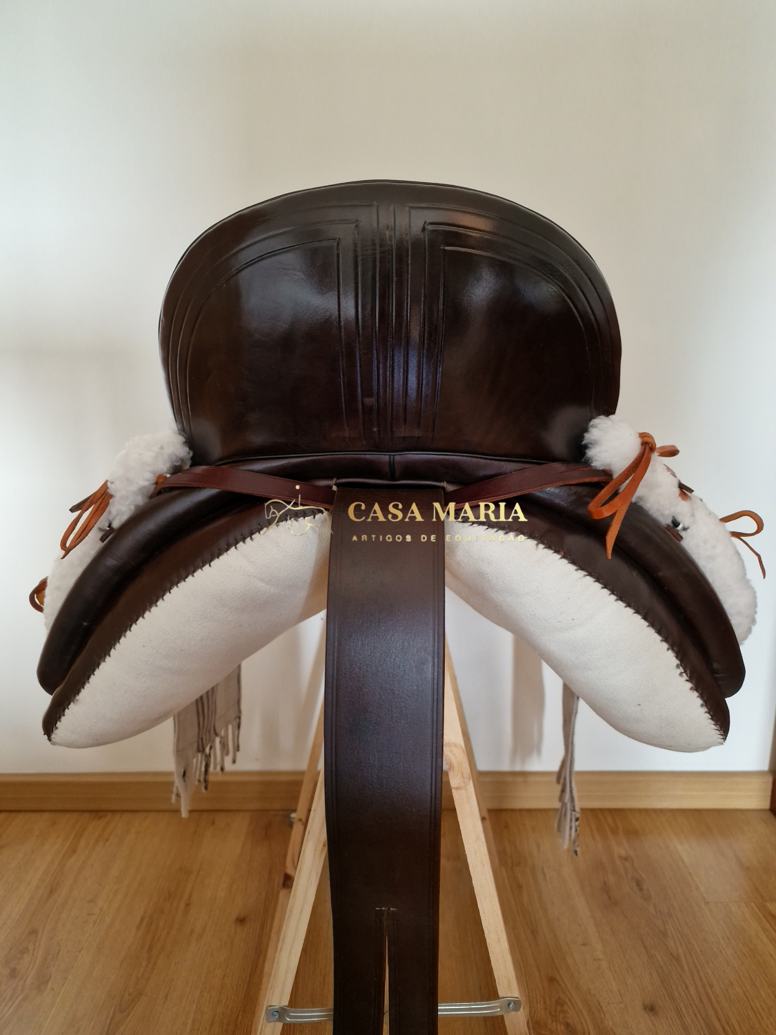 Sela de equitação em couro castanho escuro com almofadas brancas e texto Casa Maria