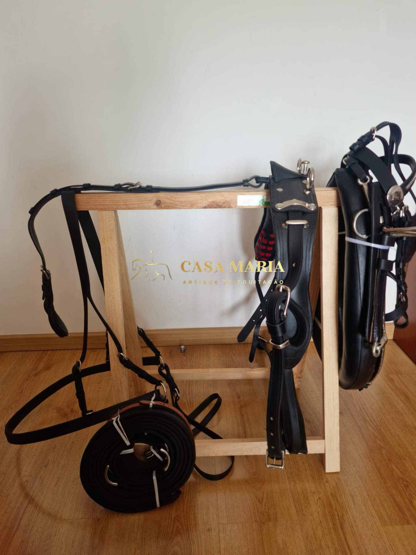 Conjunto de equipamentos de equitação em couro preto pendurados em estrutura de madeira