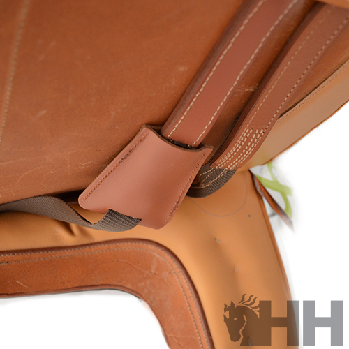 Sela de equitação em couro castanho com alças e costuras, logo 'HH' visível