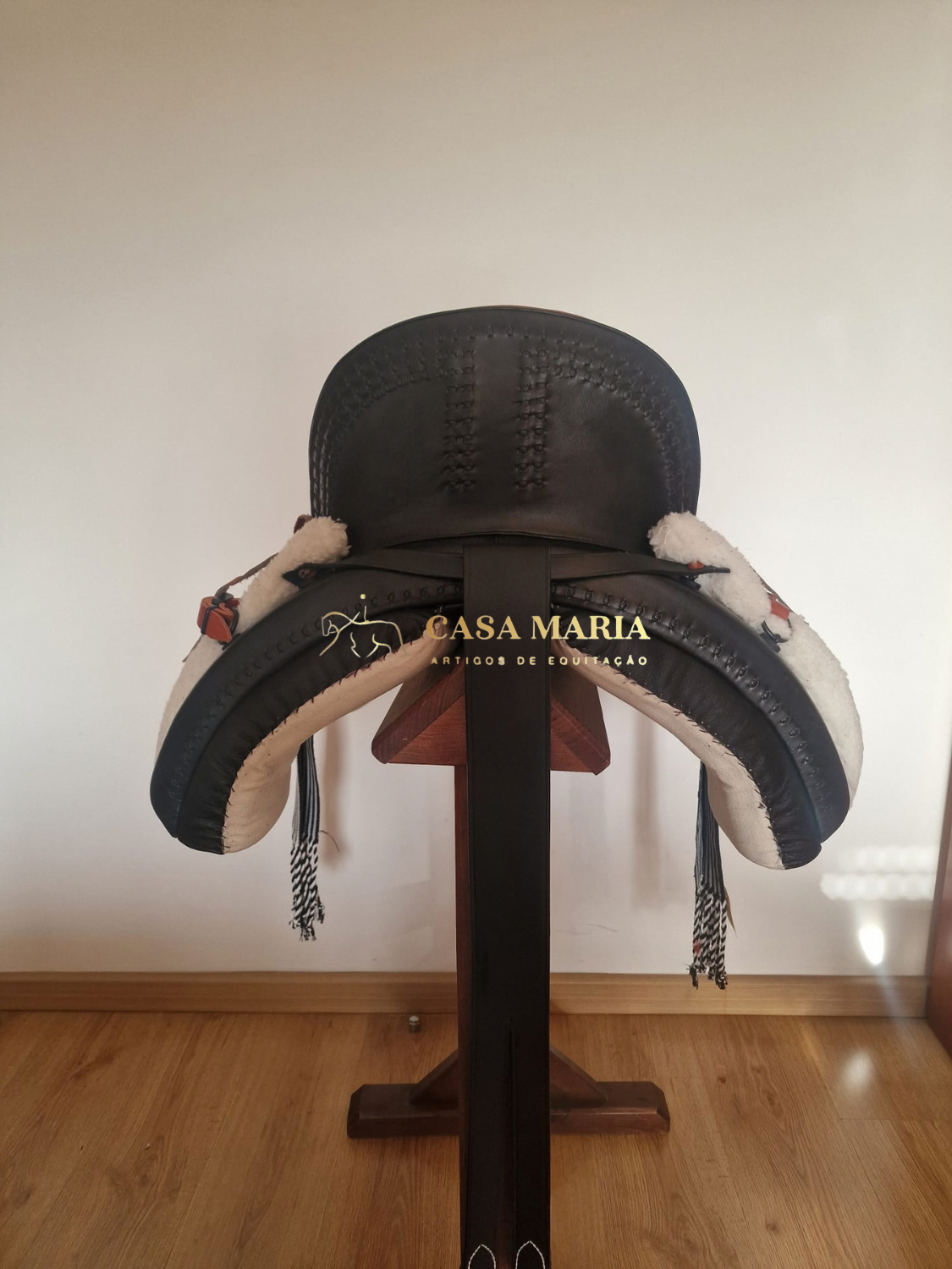 Sela de cavalo em couro preto com espuma branca nas laterais num suporte de madeira