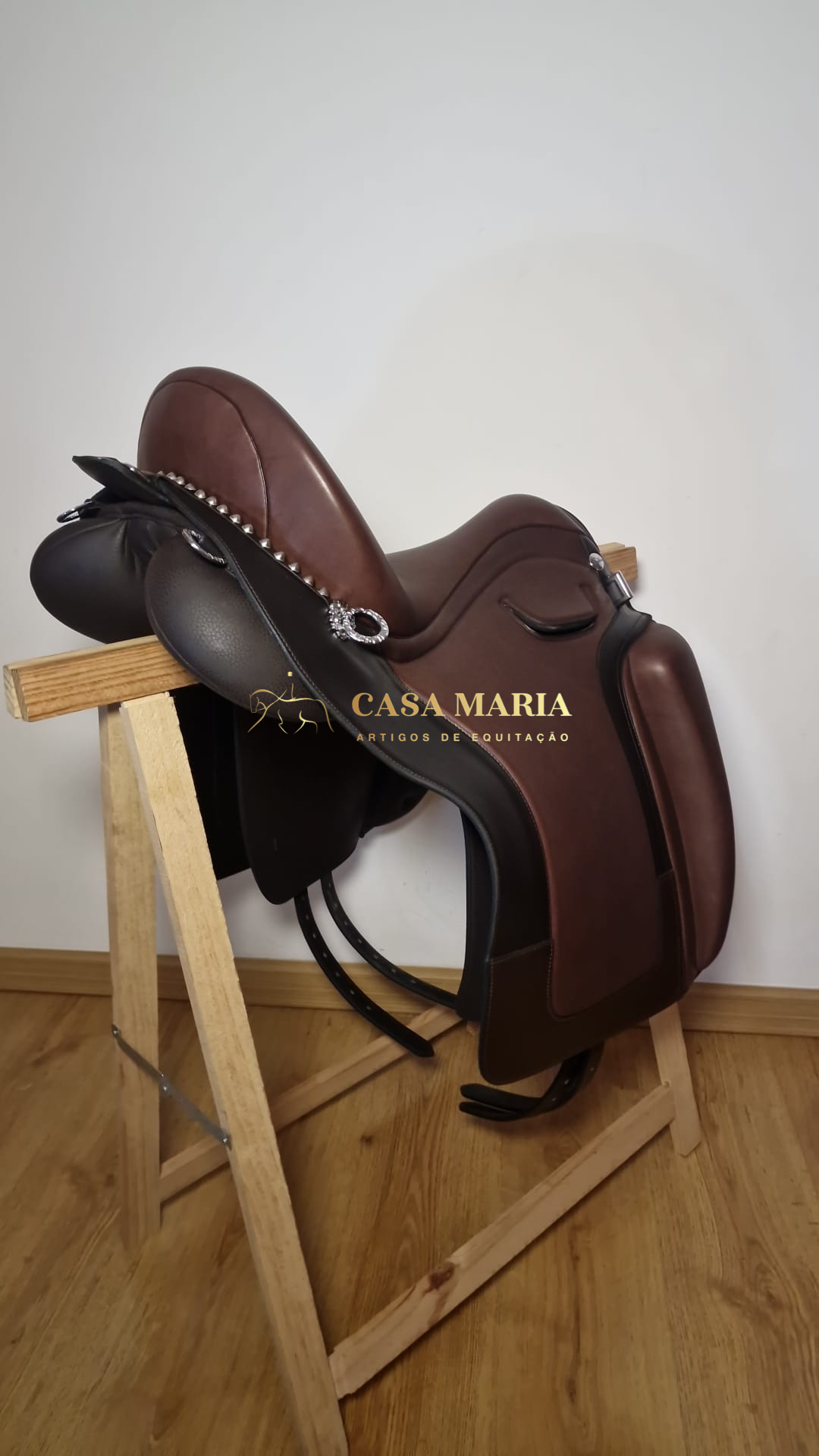 Sela de equitação castanha e preta com detalhes prateados em suporte de madeira