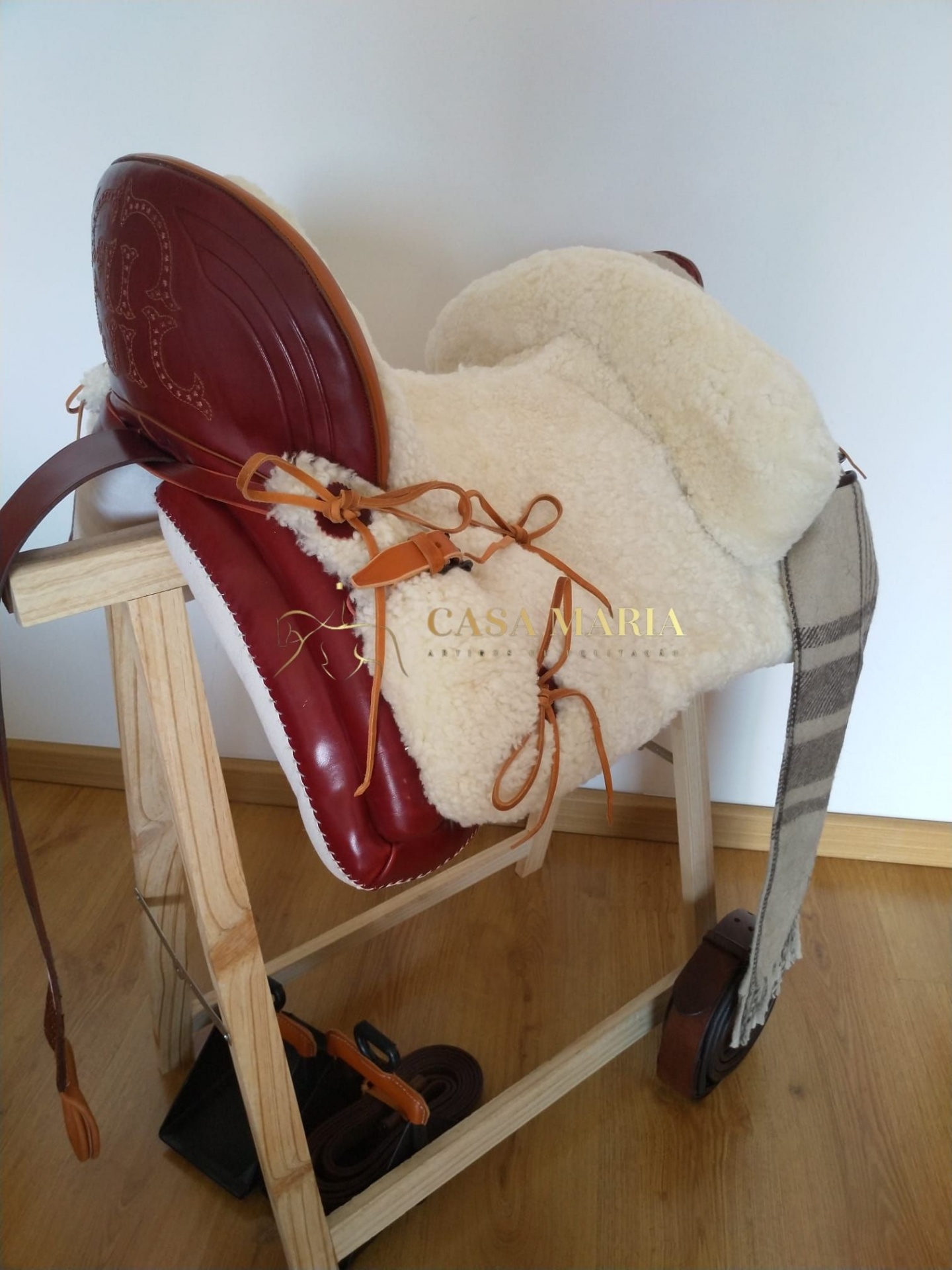 sela de equitação castanha e branca com pelo pendurada numa estrutura de madeira