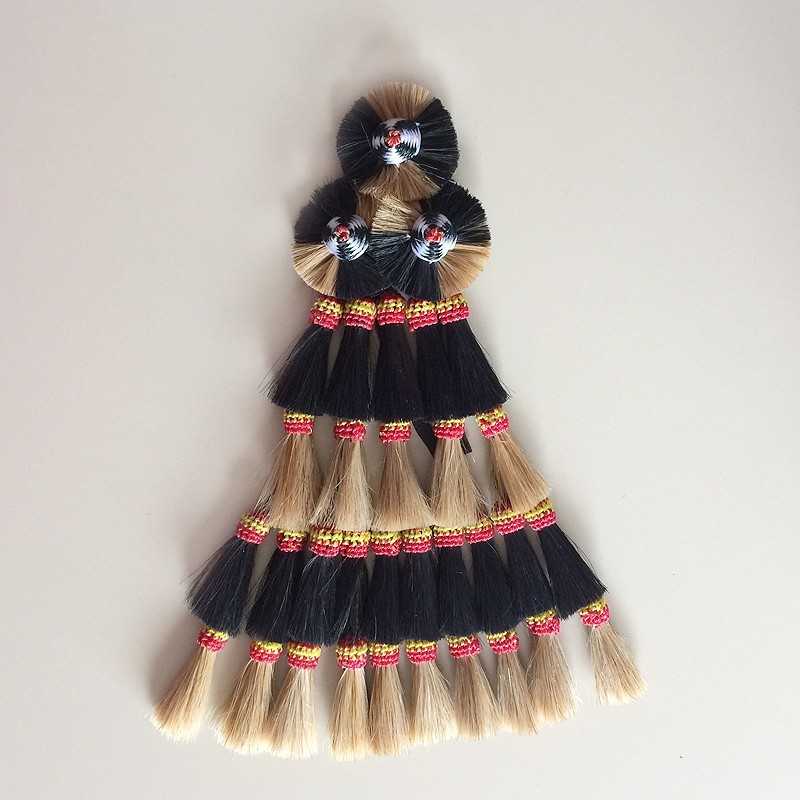 Trança decorativa com fios naturais bege e preto, amarrada com fios vermelhos e dourados.