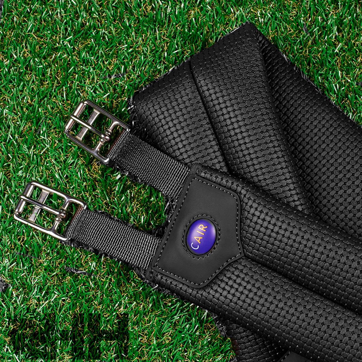 Correia preta texturizada com fivelas metálicas e etiqueta CAIF sobre relva