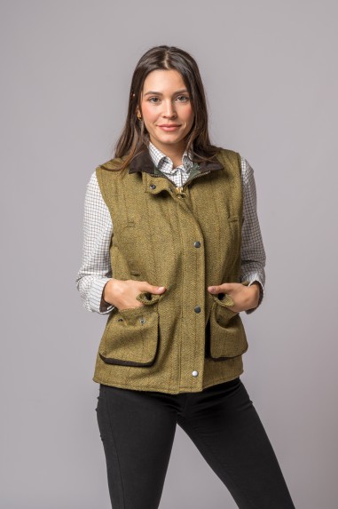 Mulher vestindo colete verde-oliva em tecido tweed com botões e bolsos, sobre camisa branca quadriculada.
