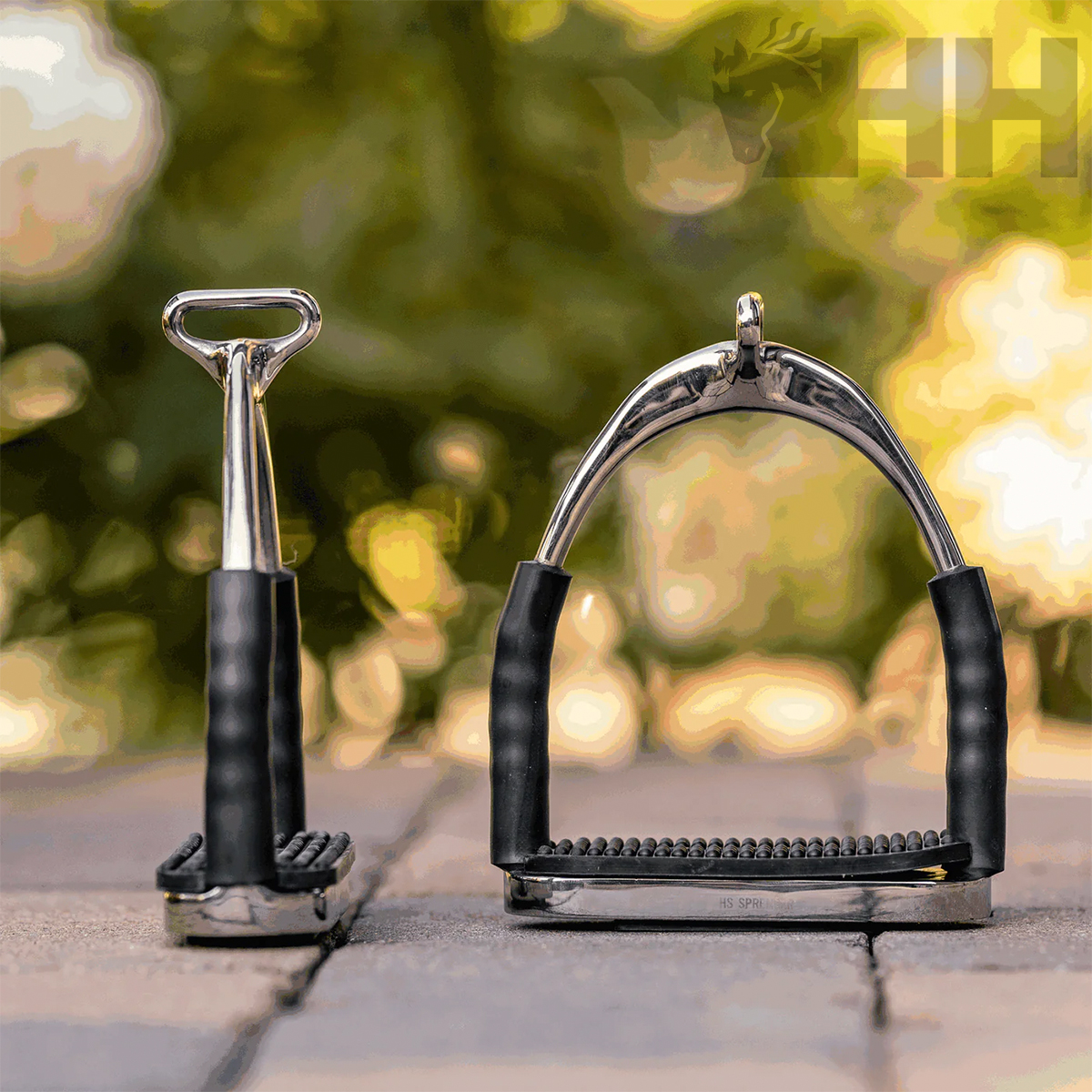 Par de estribos metálicos para equitação com empunhaduras pretas sobre pavimento exterior