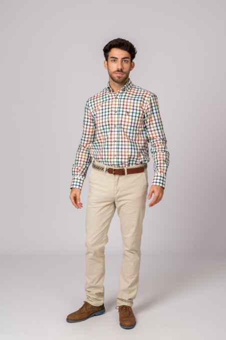 Homem com camisa xadrez colorida, calças bege, cinto castanho e sapatos castanhos em fundo cinza claro.