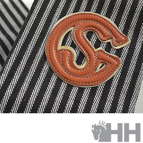 Emblema de couro com letras SG sobre tecido de riscas finas brancas e pretas