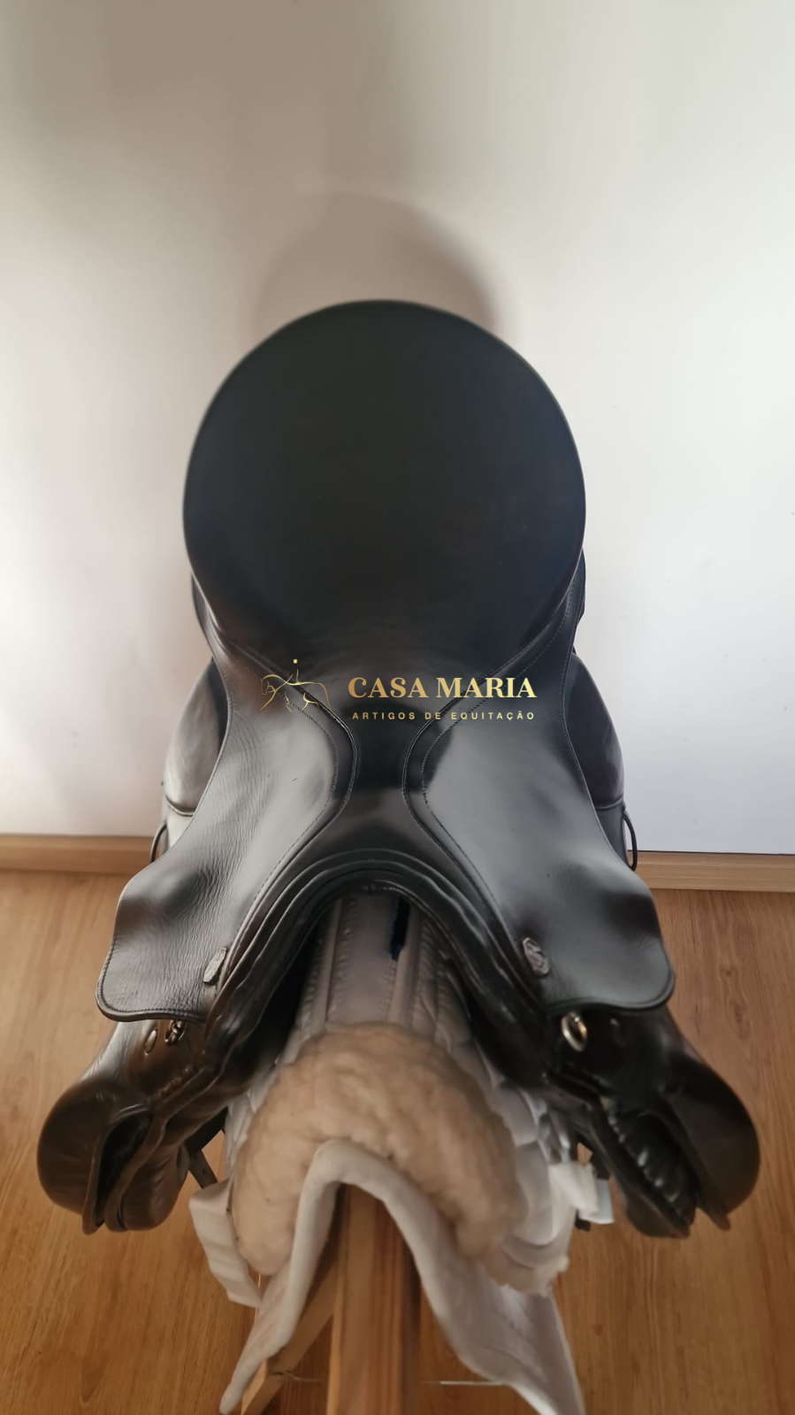 Sela de equitação em couro preto com textura lisa, sobre suporte acolchoado branco