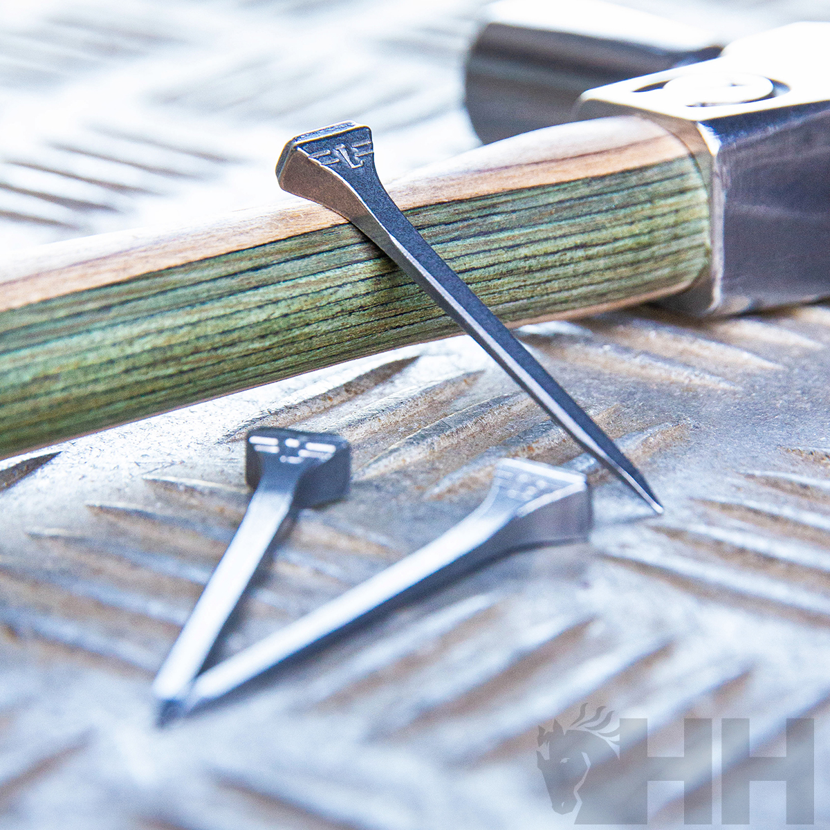 Martelo com cabo de madeira e três pregos grandes em superfície metálica