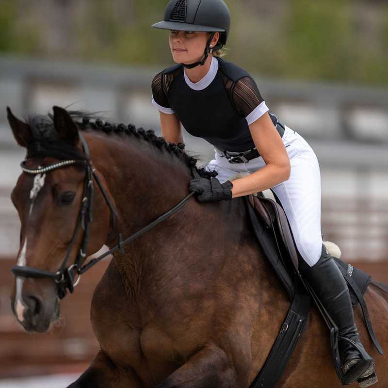 Pessoa a cavalo com roupa de equitação preta e branca e capacete preto.