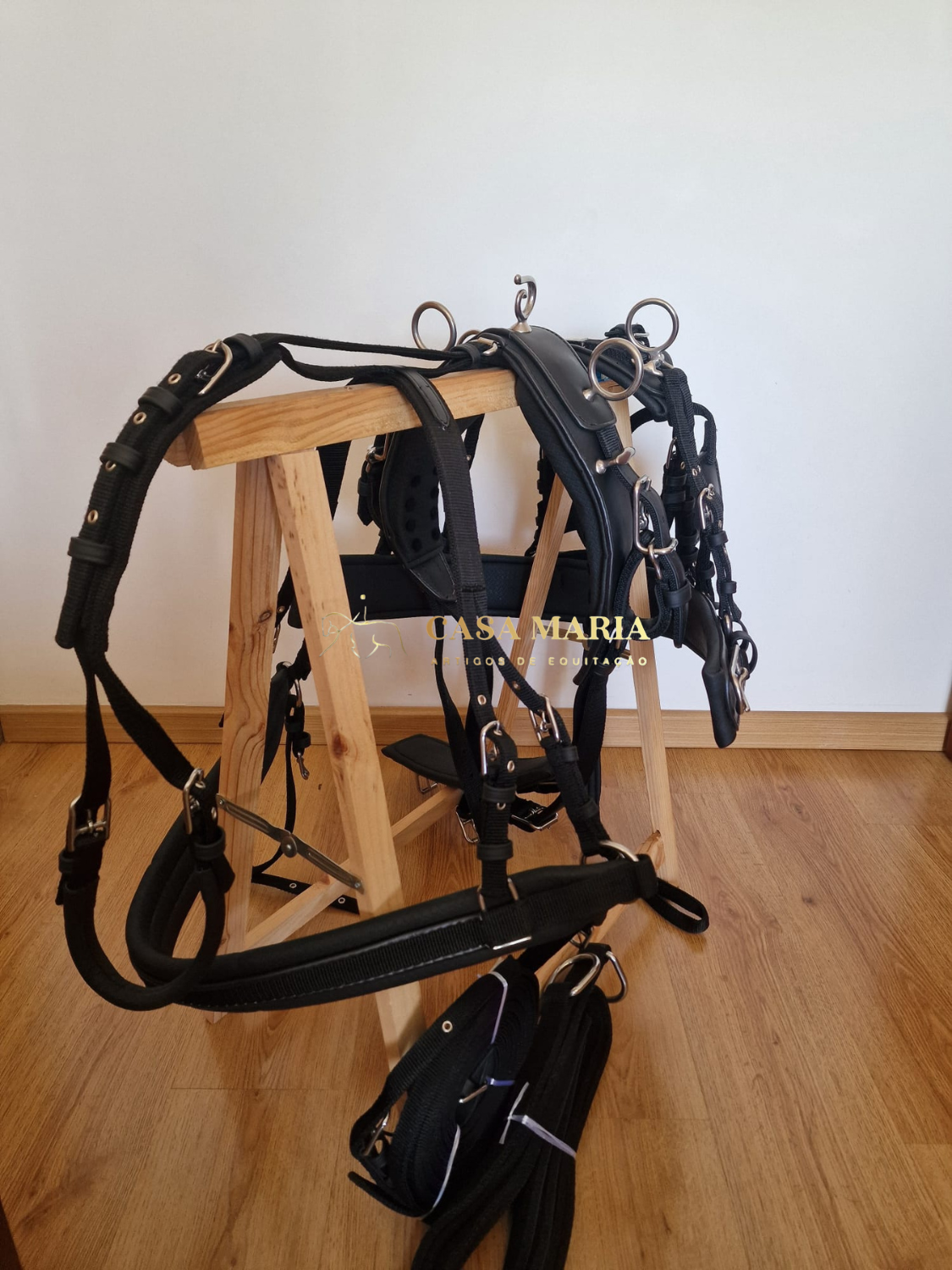 Conjunto de arreios e acessórios equestres em couro preto com ferragens metálicas prateadas num suporte de madeira