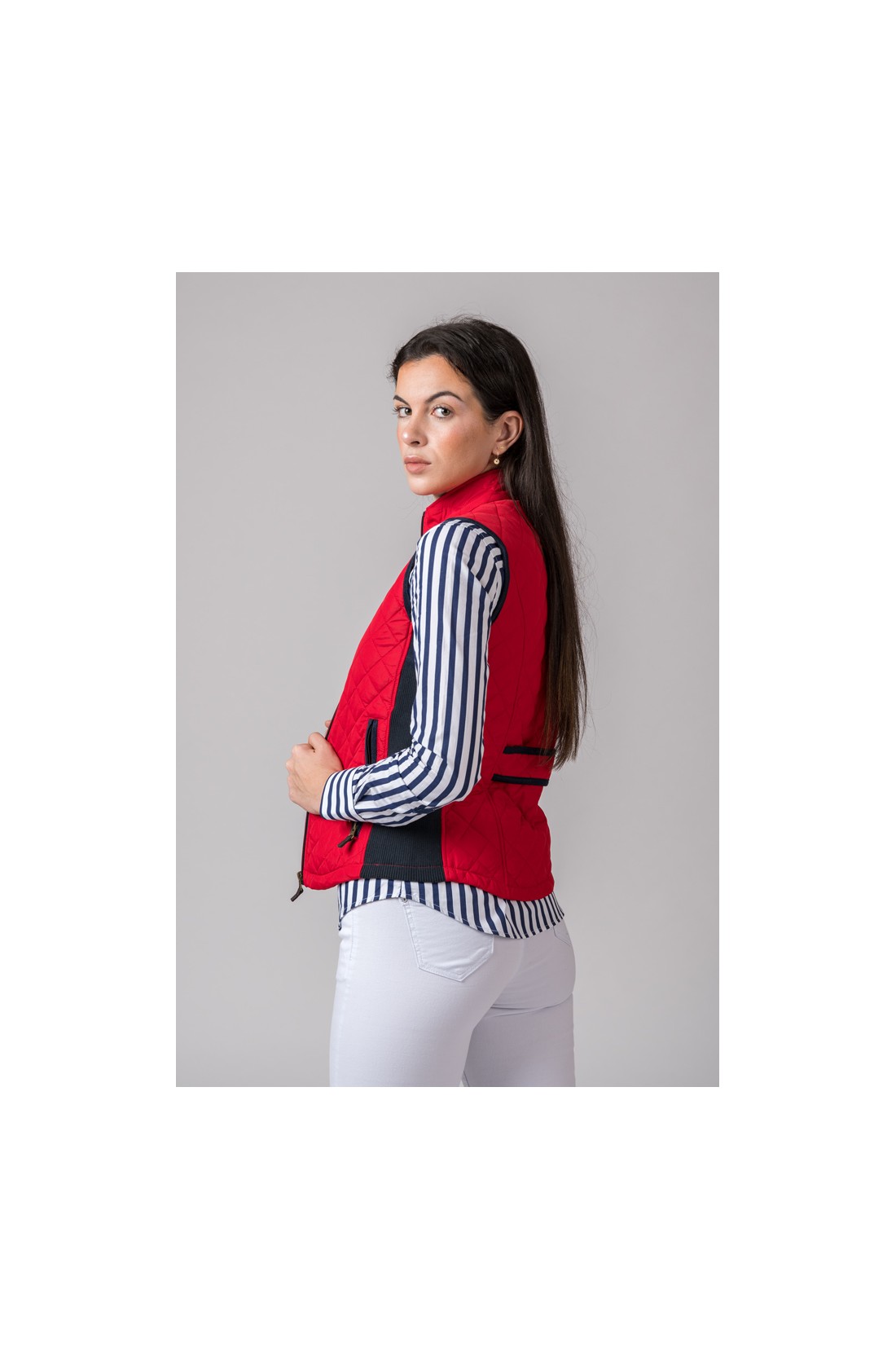 Colete vermelho acolchoado com detalhes azuis escuros usado com camisa de riscas e calças brancas.
